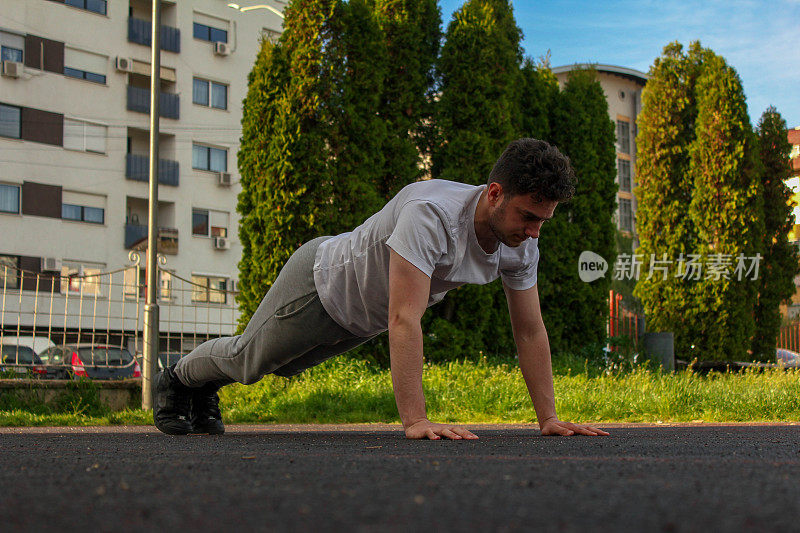 A white man jumping from the ground while doing a pushup in a public park